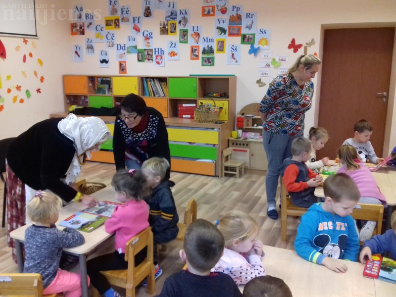 Vaikai su pasakų senele Zita Nosavičiene ir auklėtoja Emilija Bieliūniene apžiūri naujausias knygeles